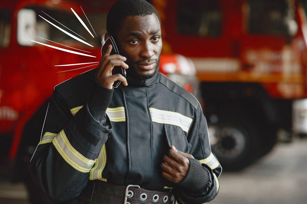 A firefighter using a cellphone with fire trucks in the background, demonstrating the role of connectivity in emergencies.